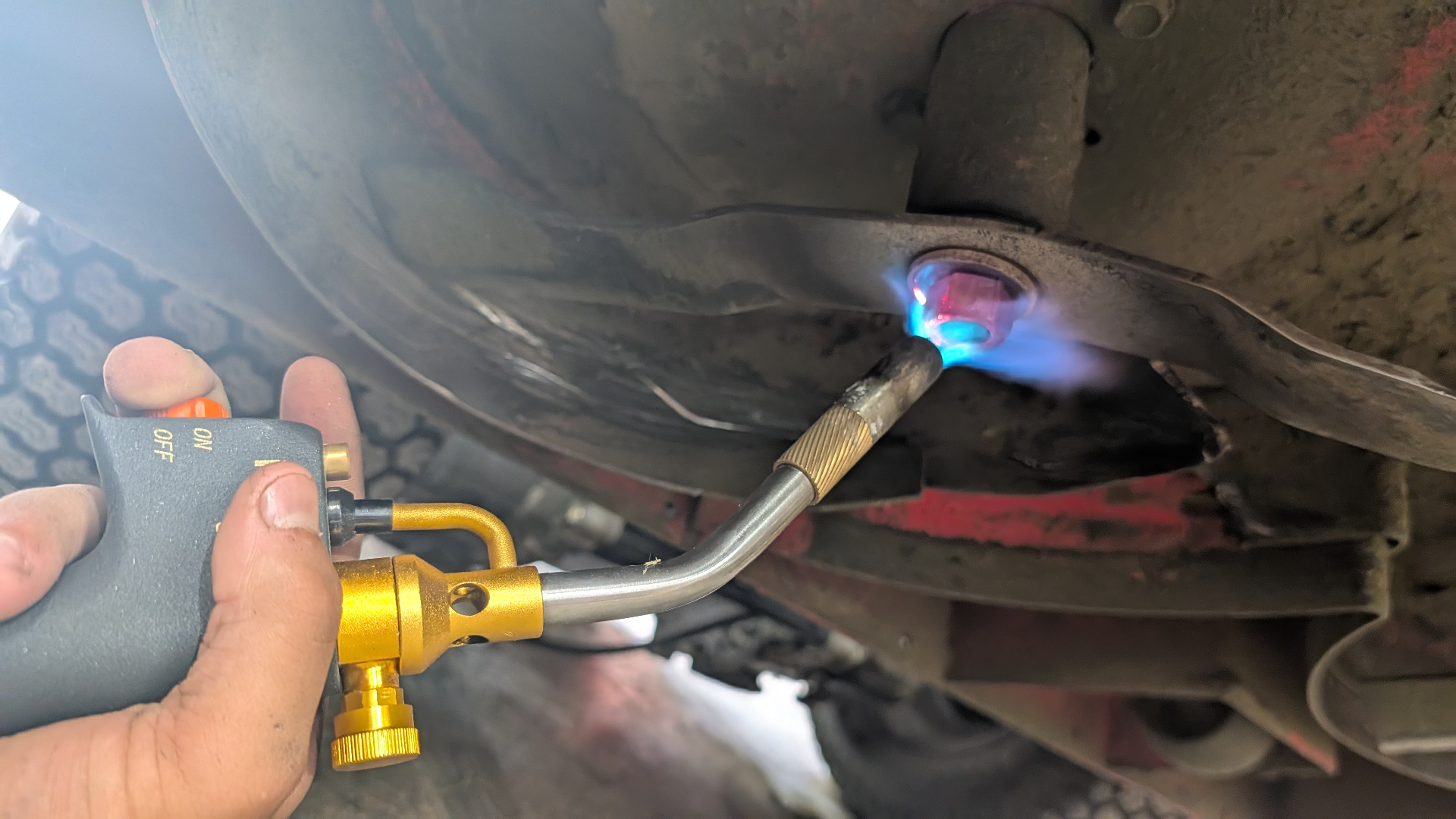 Torch heating a seized bolt under a mower deck