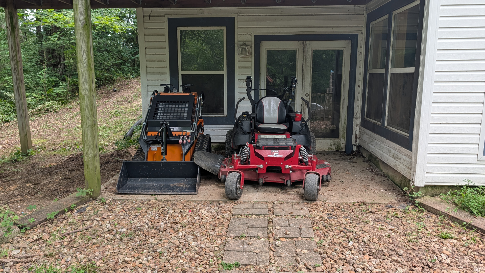Mini skid-steer loader parked next to a red zero-turn mower